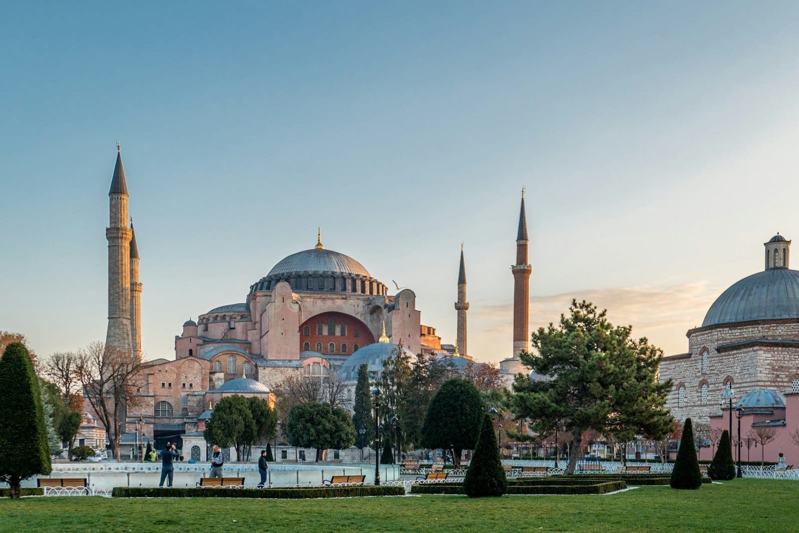 Weitwinkelansicht der Hagia Sophia in Sultanahmet mit ihren Kuppeln und Minaretten bei Sonnenuntergang, eingerahmt von grünen Gärten und klarem blauen Himmel.