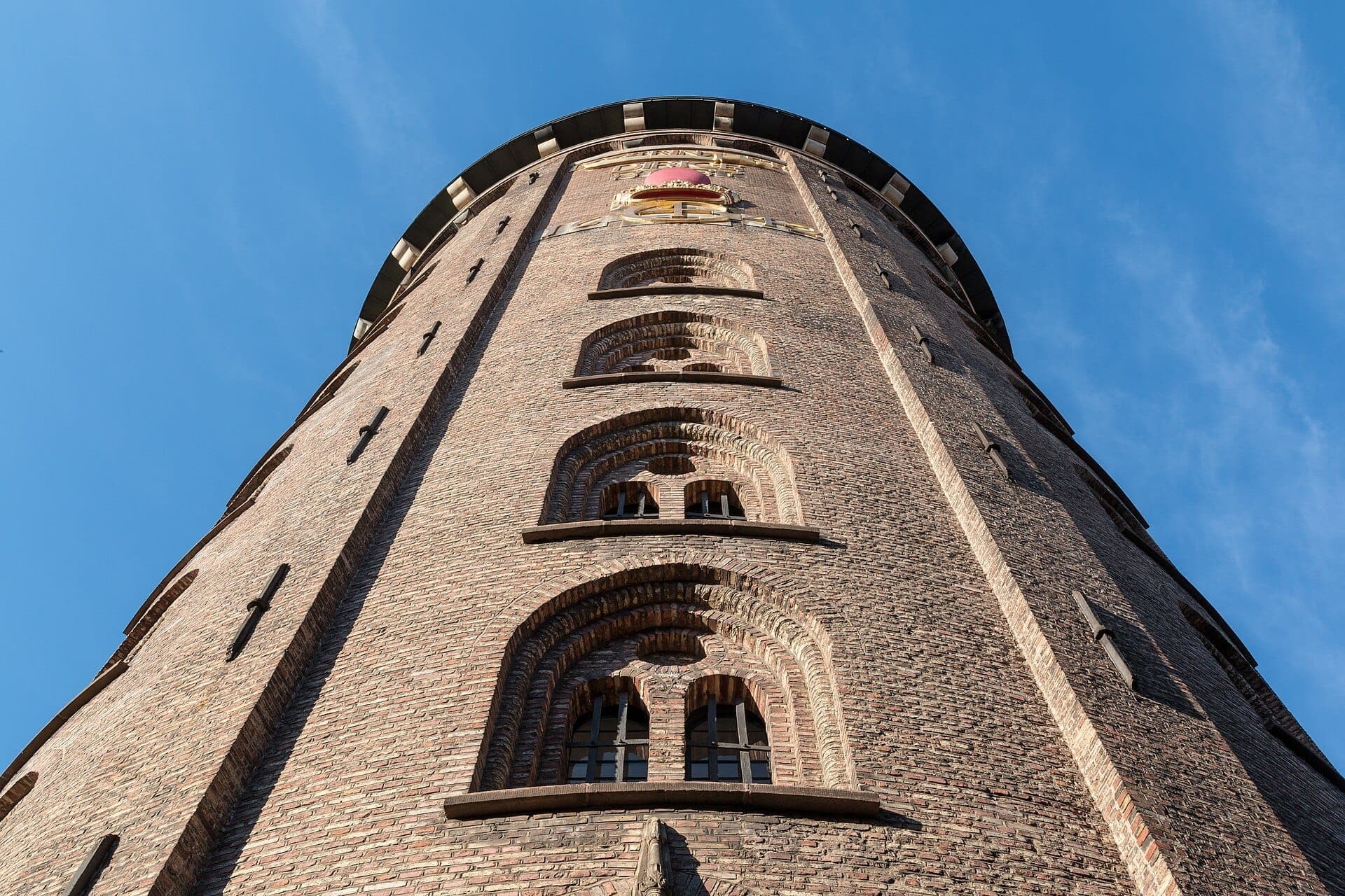 Untersicht der Backsteinassade und der Bogenfenster des Round Tower vor einem klaren blauen Himmel über Kopenhagen.
