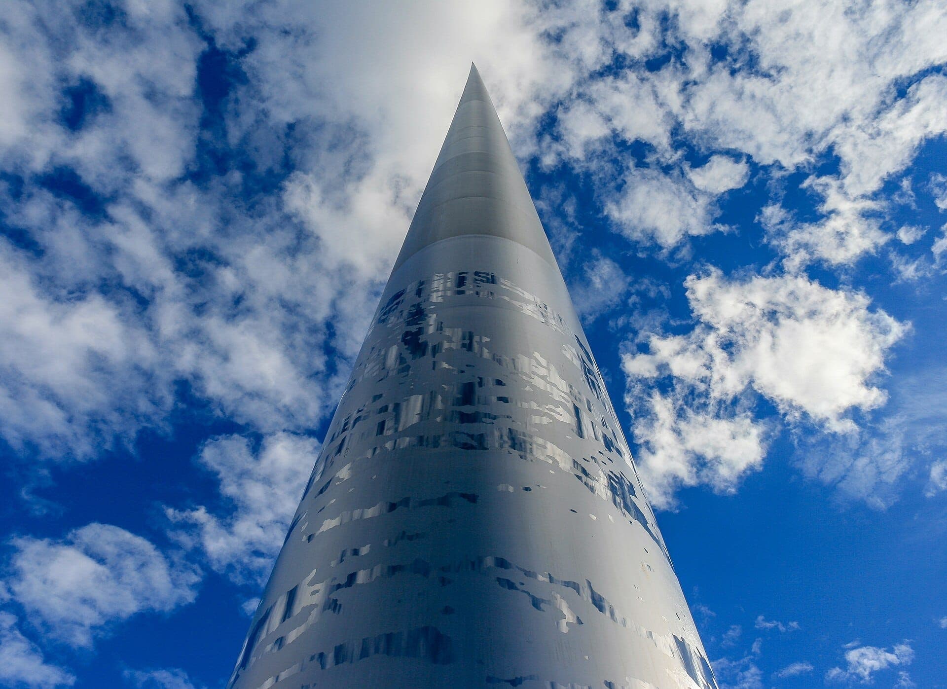 Вид снизу вверх на монумент Spire of Dublin на фоне ярко-голубого неба с редкими белыми облаками днём.