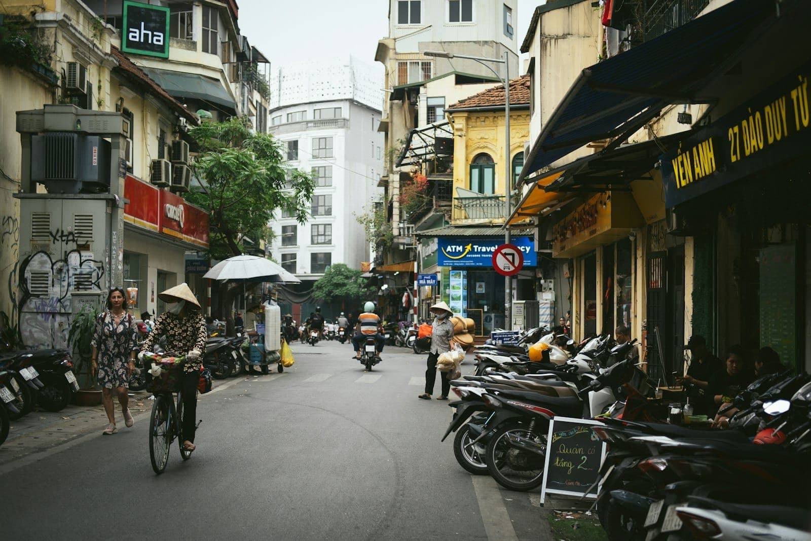 Phố phường Hà Nội nhộn nhịp với người đi bộ, xe máy và những quán cà phê vỉa hè, hai bên là những tòa nhà thuộc địa sơn vàng cao tầng và các cửa hiệu san sát.