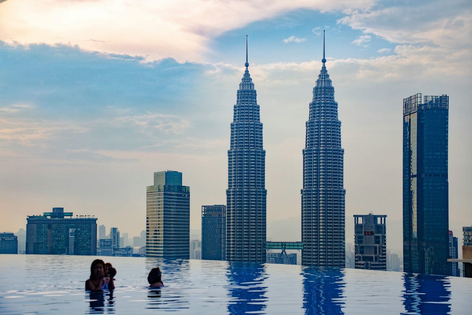 Hồ bơi vô cực với mọi người thưởng thức tầm nhìn ra đường chân trời Kuala Lumpur, nổi bật với Petronas Twin Towers lúc hoàng hôn.