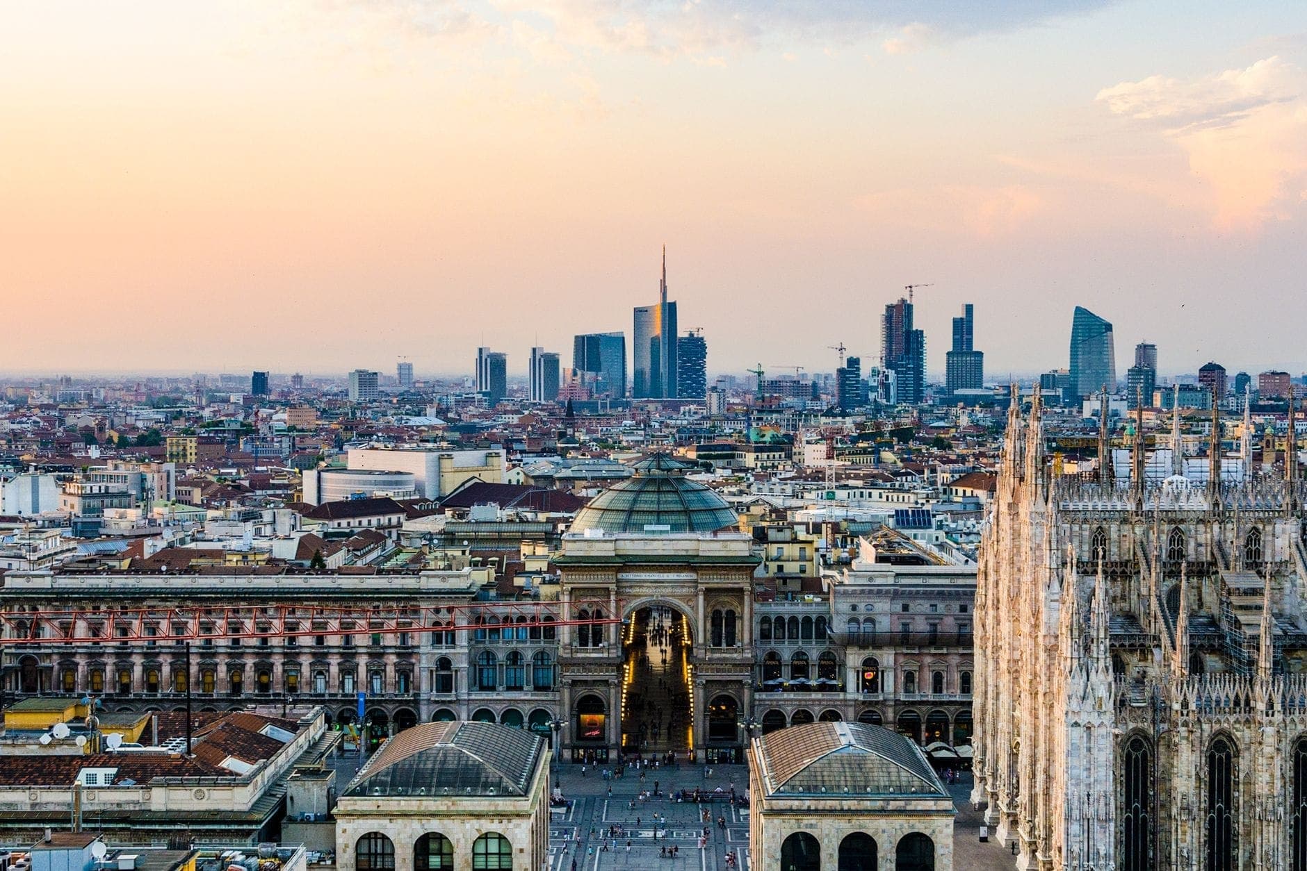 Vista aérea amplia de Milán con el Duomo, la Galleria Vittorio Emanuele II y rascacielos modernos al atardecer.