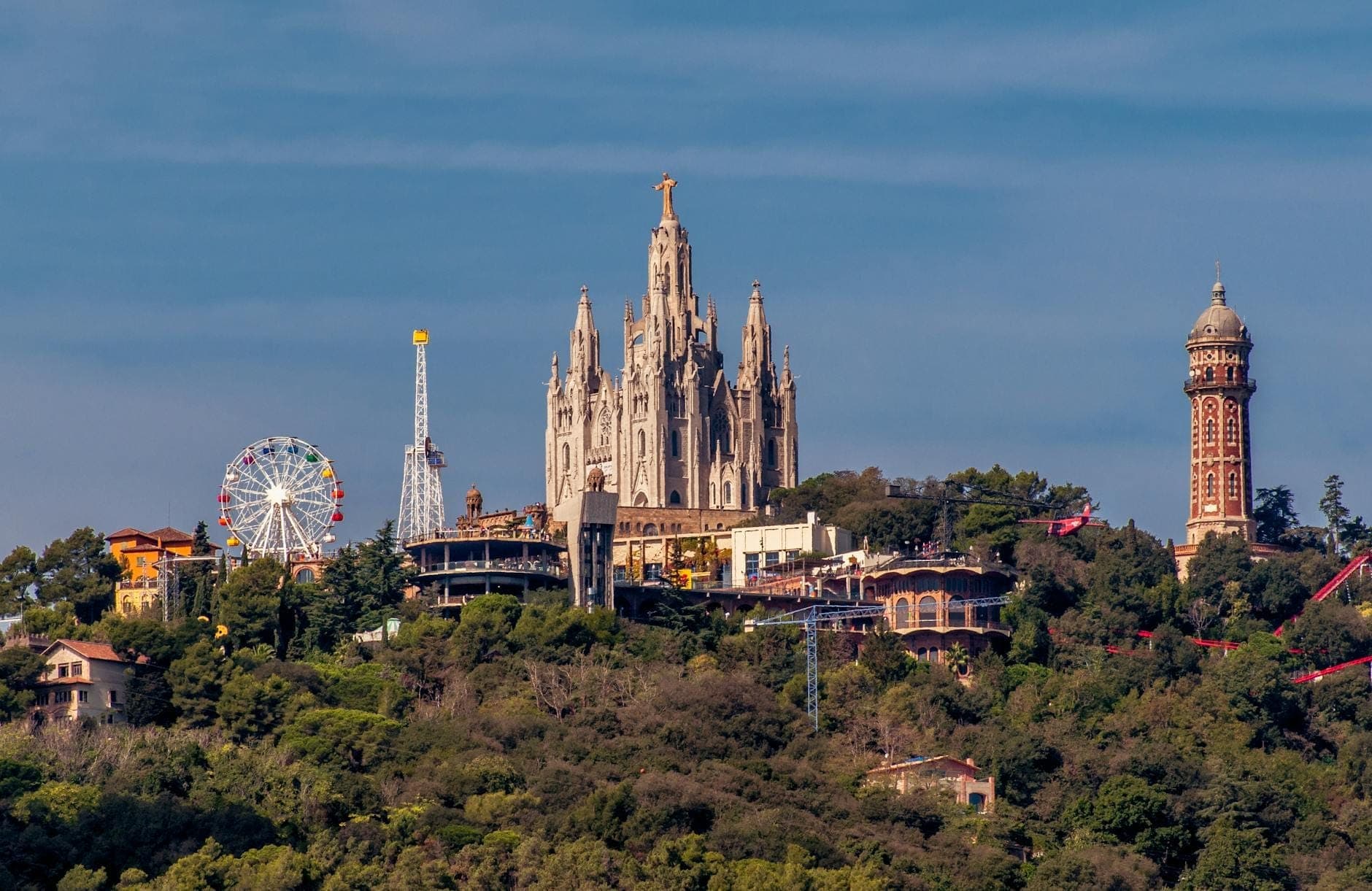 Toàn cảnh đồi Tibidabo với Temple Expiatori del Sagrat Cor, những trò chơi hội chợ cổ điển và mảng xanh tươi tốt dưới bầu trời xanh trong.