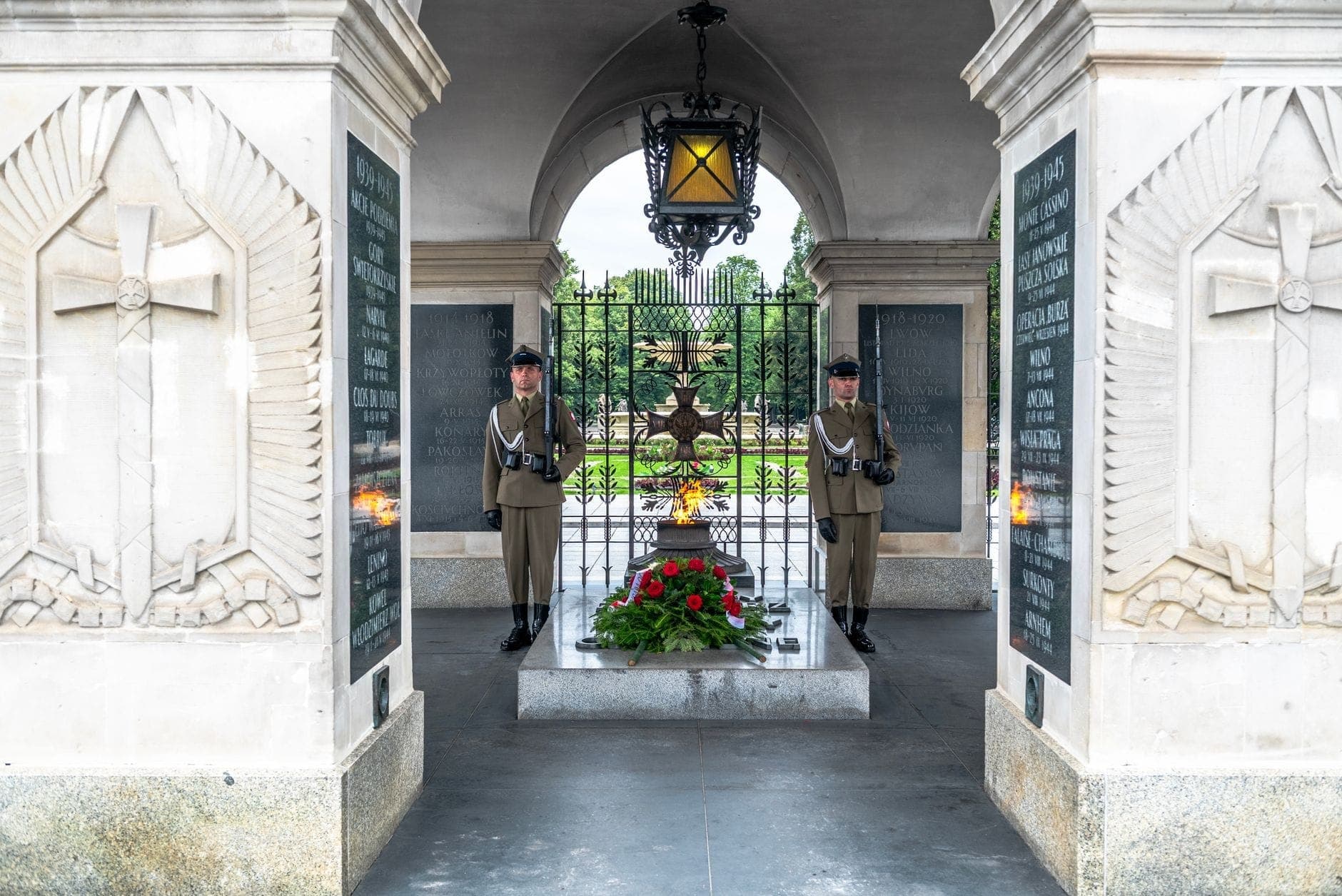 Zwei uniformierte Wachen stehen stramm neben dem Grab des Unbekannten Soldaten unter der steinernen Arkade in Warschau, im Vordergrund Blumen und die ewige Flamme.
