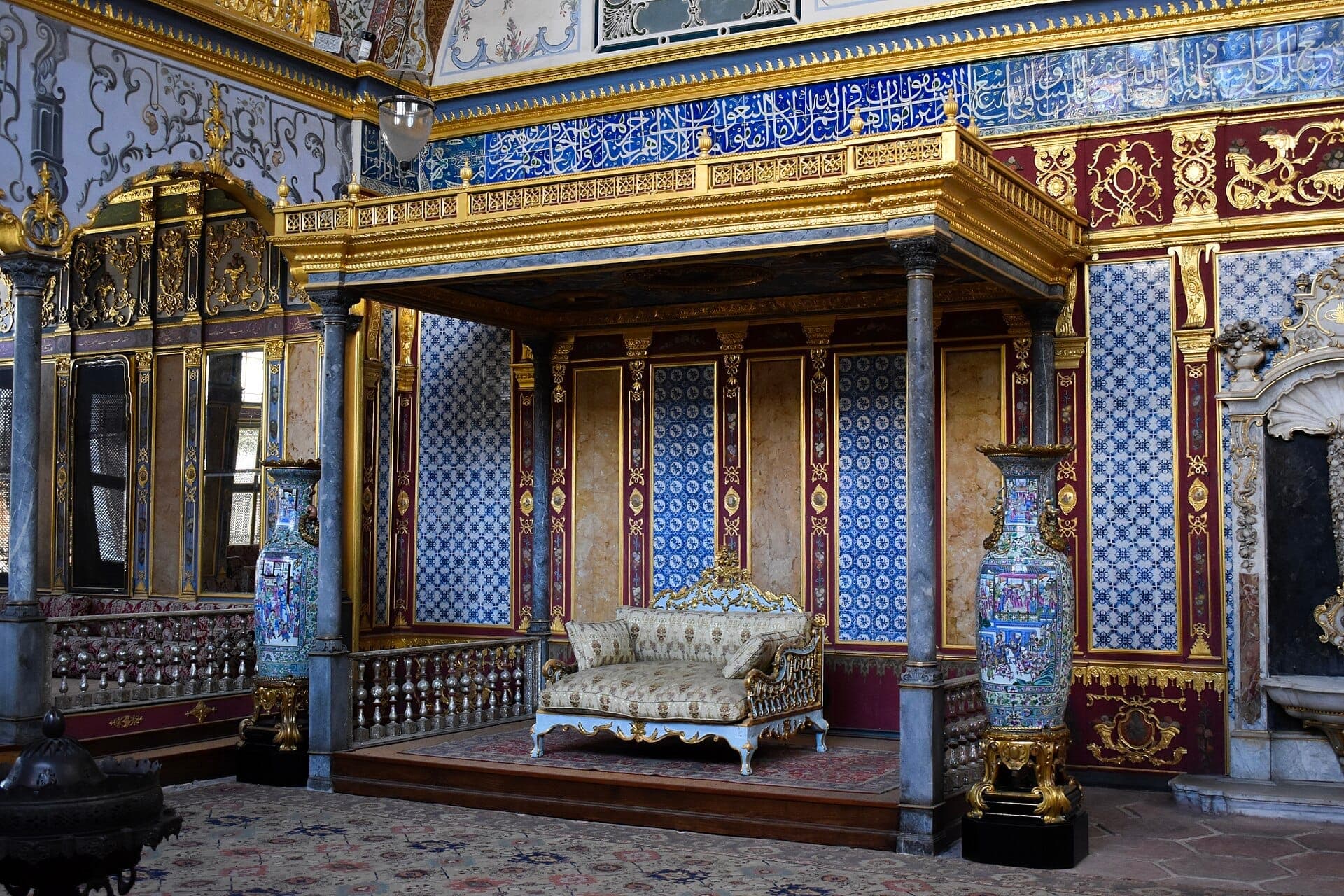 Der prächtige Audienzsaal im Harem des Topkapı-Palastes mit goldener Dekoration, gemusterten blauen Kacheln, Marmorsäulen und einem eleganten Sofa als Mittelpunkt.