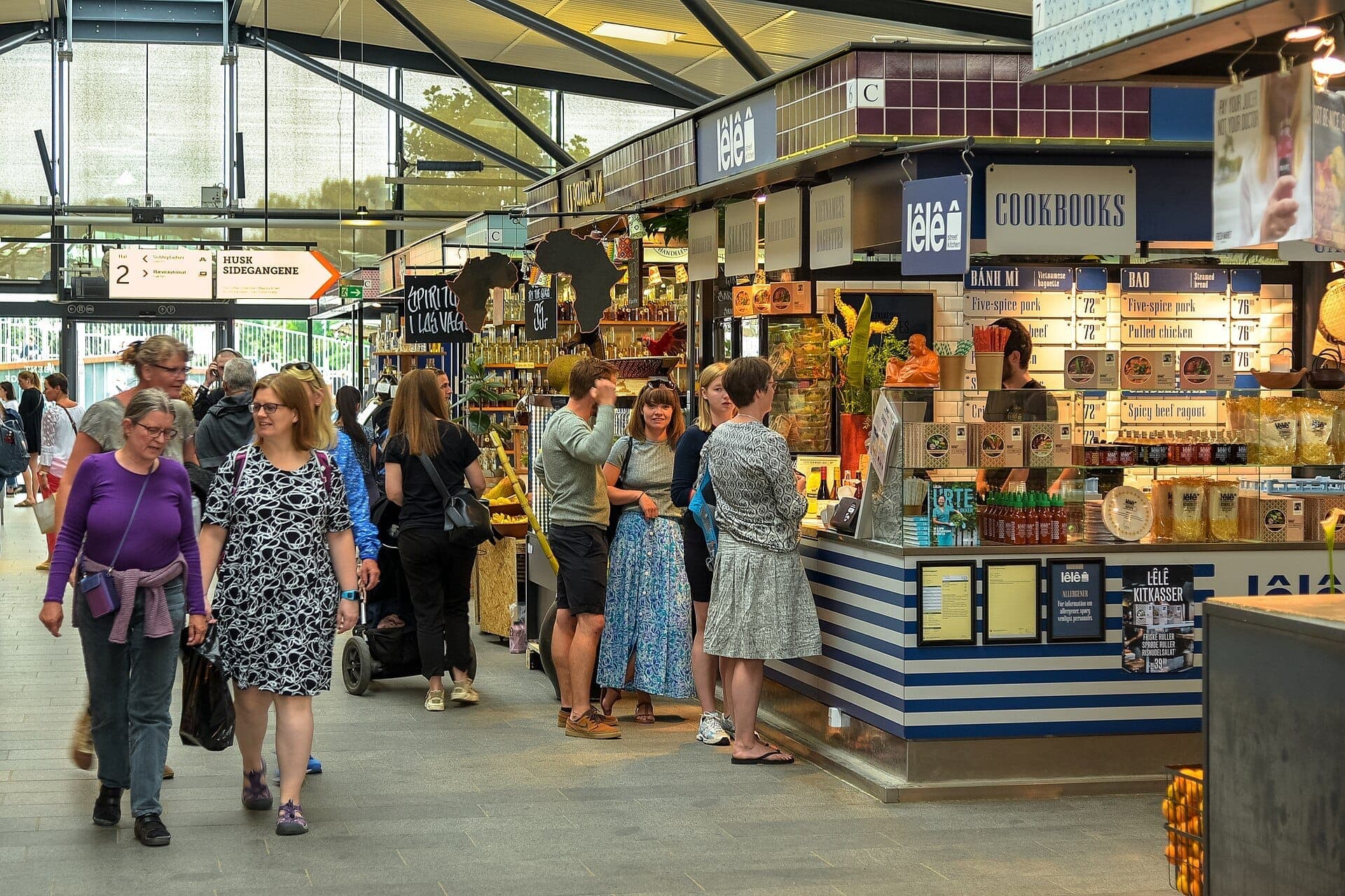 Besucher erkunden verschiedene Essensstände und Händler im hellen, lebhaften Lebensmittelmarkt Torvehallerne in Kopenhagen, Dänemark.