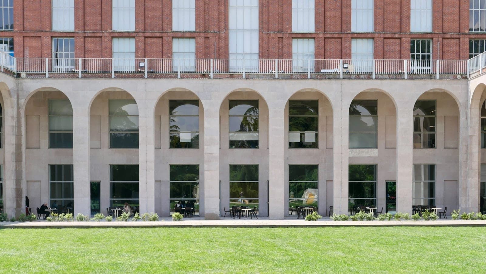 Facade of the Triennale Milano Design Museum with grand arches, large windows, and a green lawn in front under daylight.
