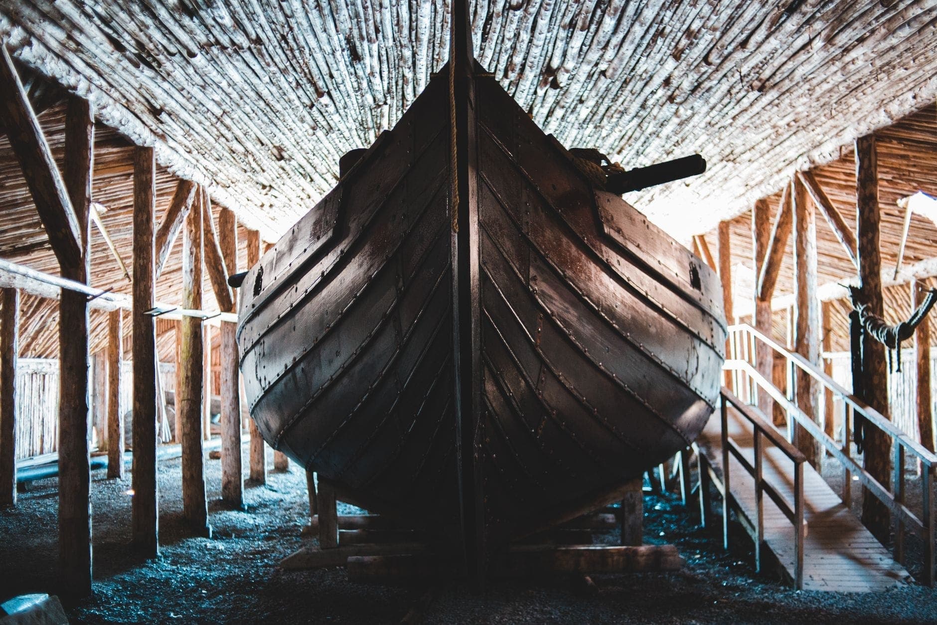 Interno della sala delle navi vichinghe in legno: lo scafo conservato di un'imbarcazione millenaria visto dalla prua, circondato da travi rustiche in legno.