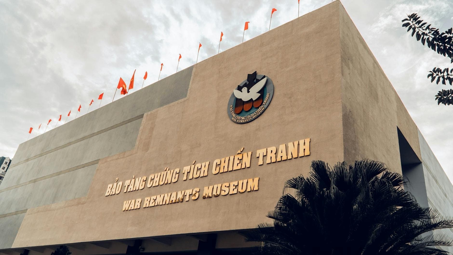 Mặt tiền Bảo tàng Chứng tích Chiến tranh với tên bảo tàng bằng cả tiếng Việt và tiếng Anh, chụp từ phía dưới với bầu trời ấn tượng phía sau.