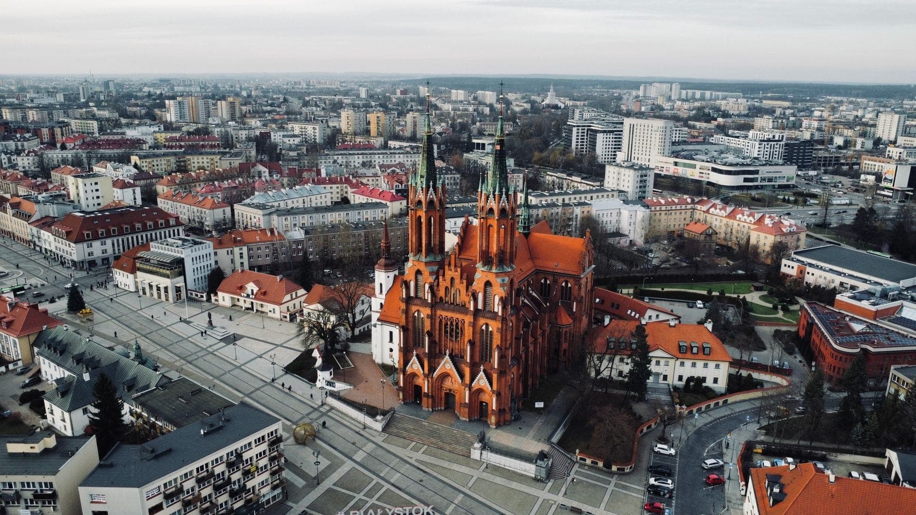 Luftaufnahme einer markanten neugotischen Kirche aus rotem Backstein mit hohen Türmen, umgeben von städtischen Gebäuden in Warschau.