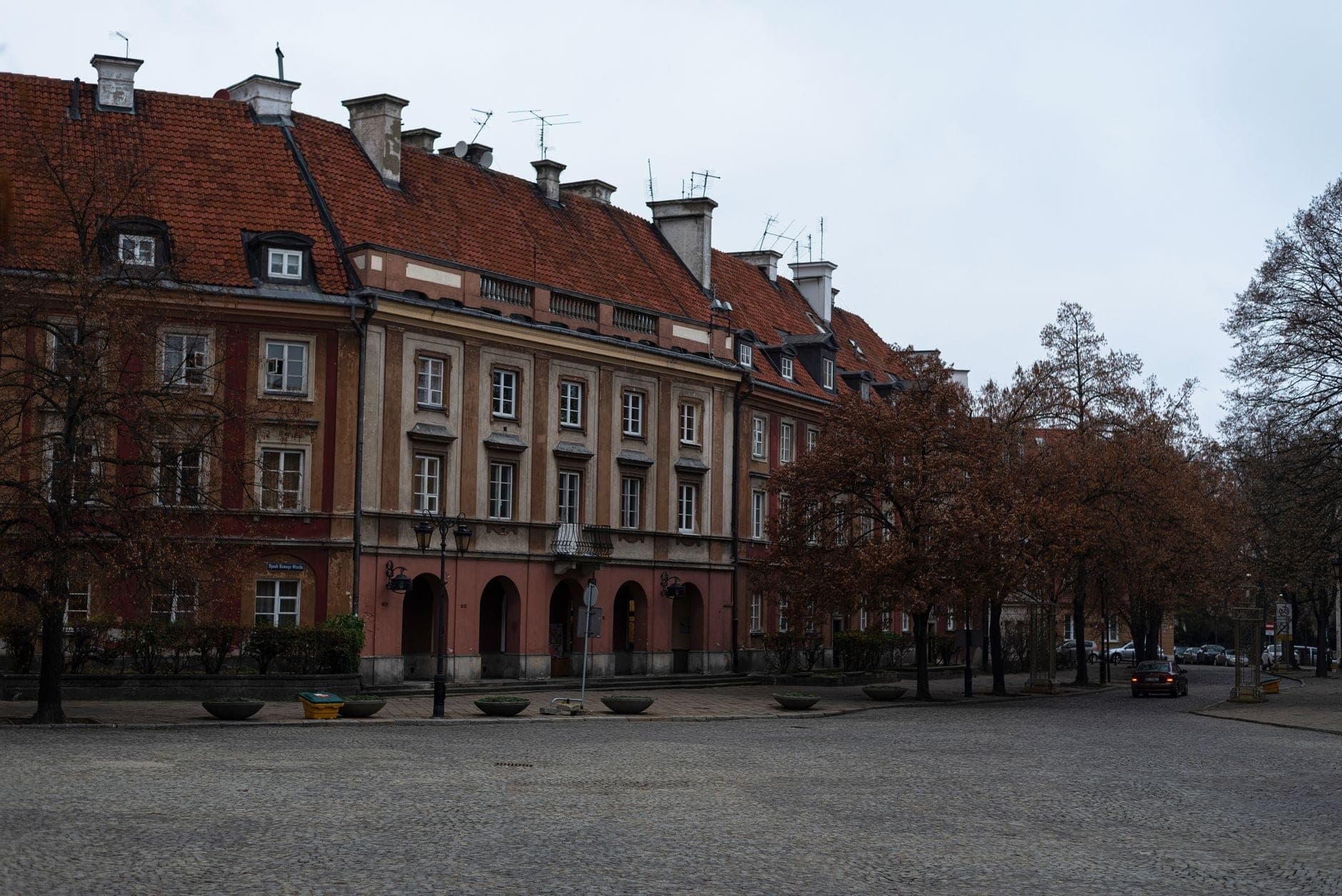 Eine Reihe historischer Vorkriegs-Mietskasernen mit roten Ziegeldächern, Kopfsteinpflasterstraße und Herbstbäumen in einem authentischen Warschauer Stadtviertel.