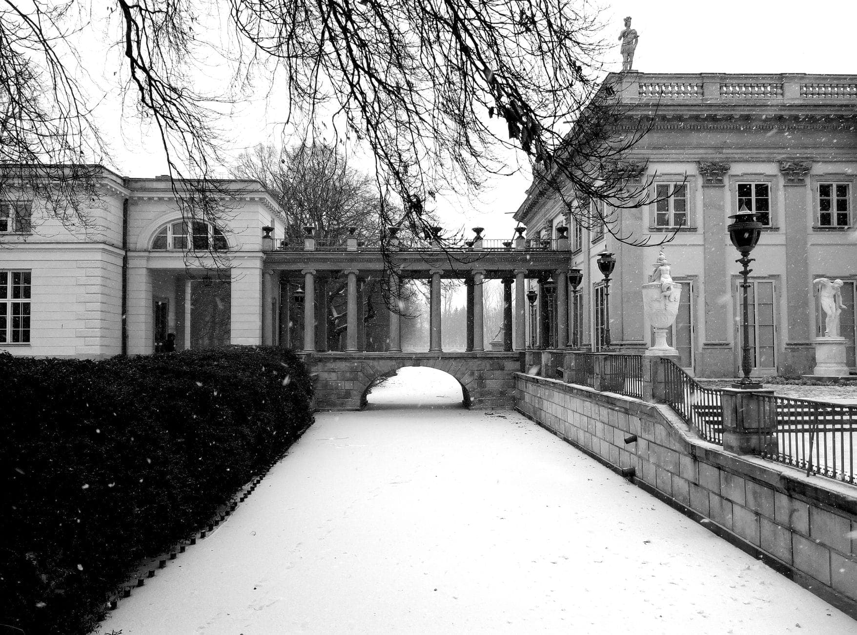 Schwarz-Weiß-Foto des Palastes im Łazienki-Park in Warschau mit frischem Schnee auf dem Boden und sichtbarer klassischer Architektur.