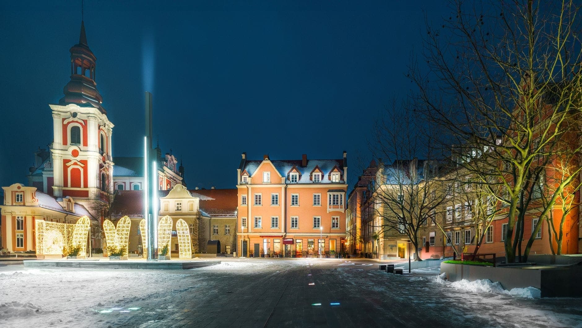 Altstadtplatz von Warschau bei Nacht mit Schnee auf dem Boden, beleuchteten historischen Gebäuden und Kirchtürmen unter einem dunklen Winterhimmel.