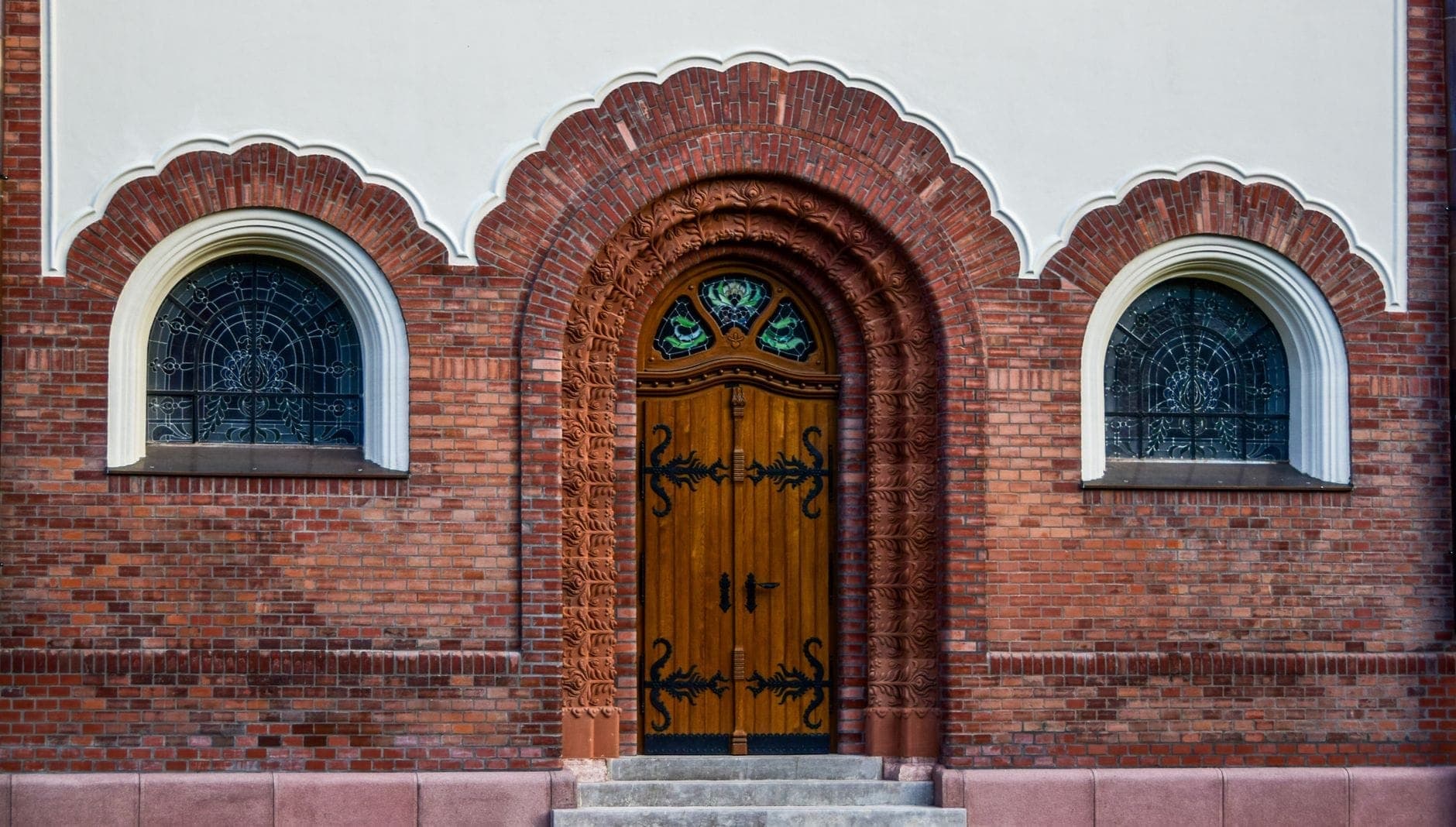 Primo piano dell'ornato ingresso in mattoni ad arco della Sinagoga Nożyk a Varsavia, con finestre decorative e una porta in legno.