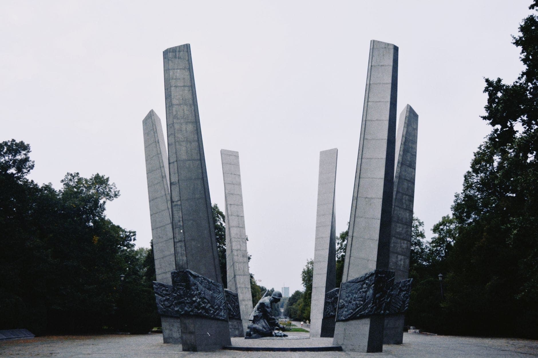 Weitwinkelperspektive auf das Denkmal der Ghettohelden in Warschau, eingerahmt von hohen Betonsäulen und Bäumen – eine der wichtigsten Gedenkstätten der jüdischen Geschichte der Stadt.