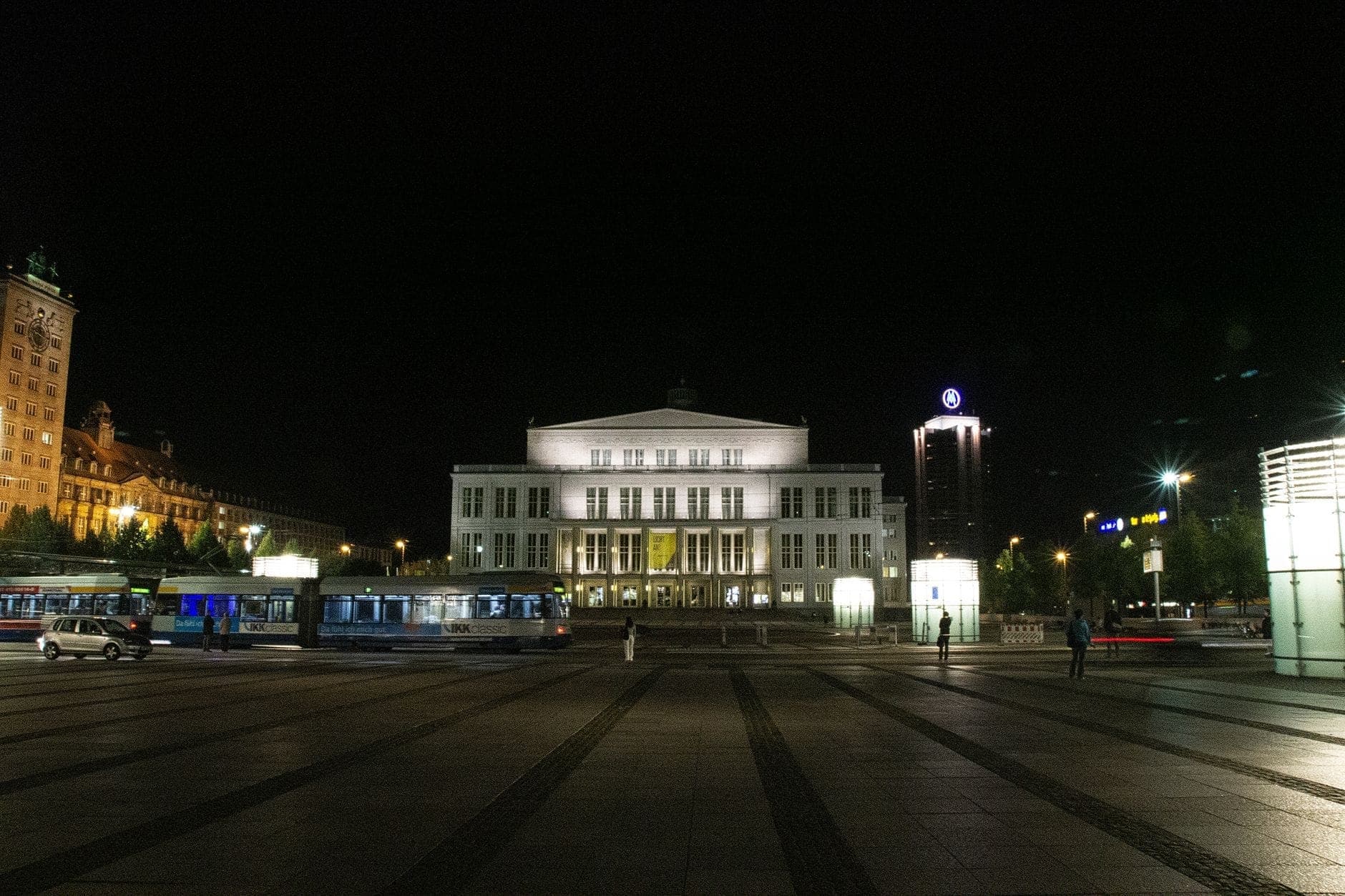 Nächtliche Ansicht des beleuchteten Grand Theatre in Warschau, mit einem ruhigen Platz und wenigen Menschen in der Umgebung.