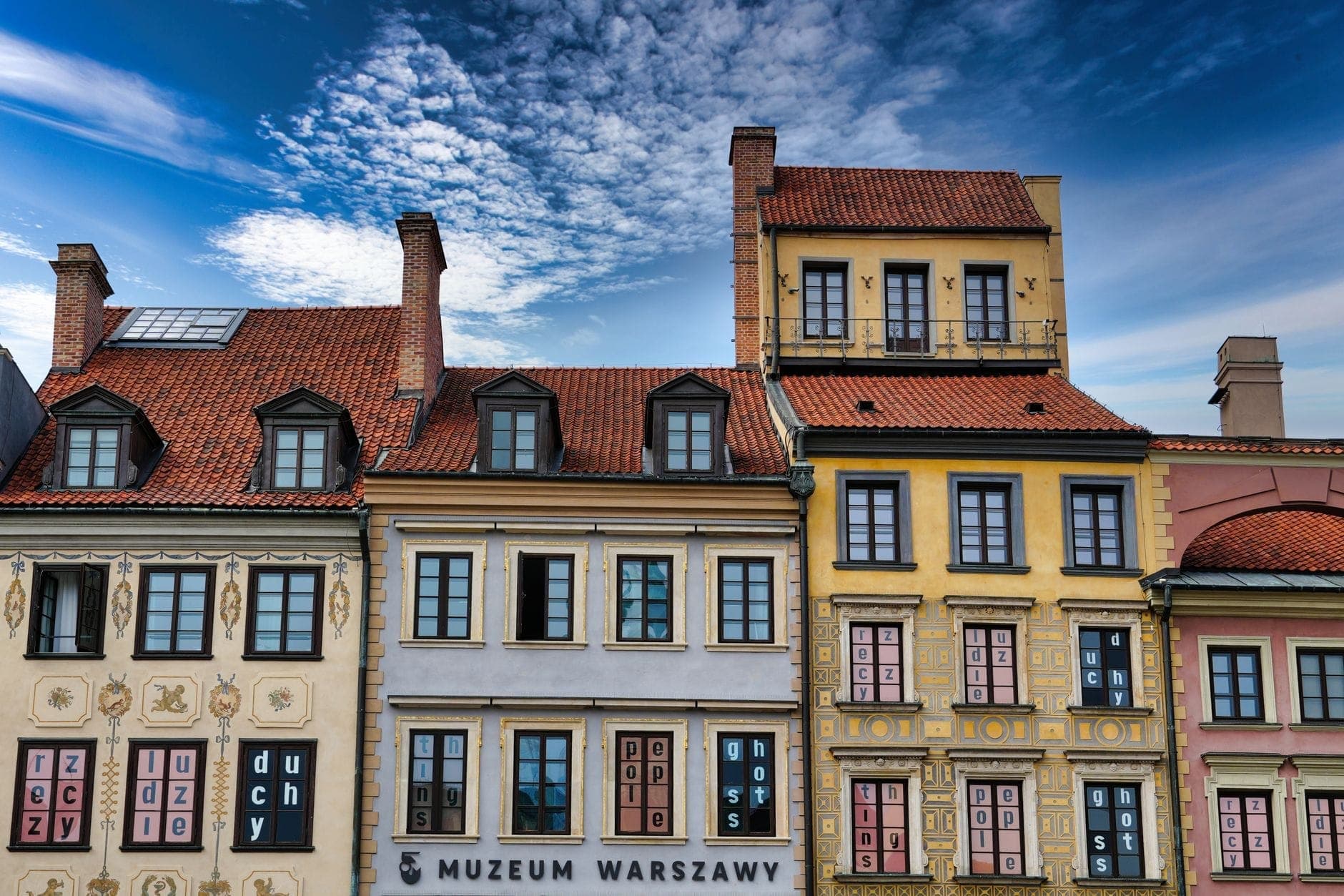 Farbenfrohe historische Gebäude mit verzierten Fassaden unter einem strahlend blauen Himmel in der Warschauer Altstadt, mit dem Schild des Warschauer Museums auf Straßenniveau.