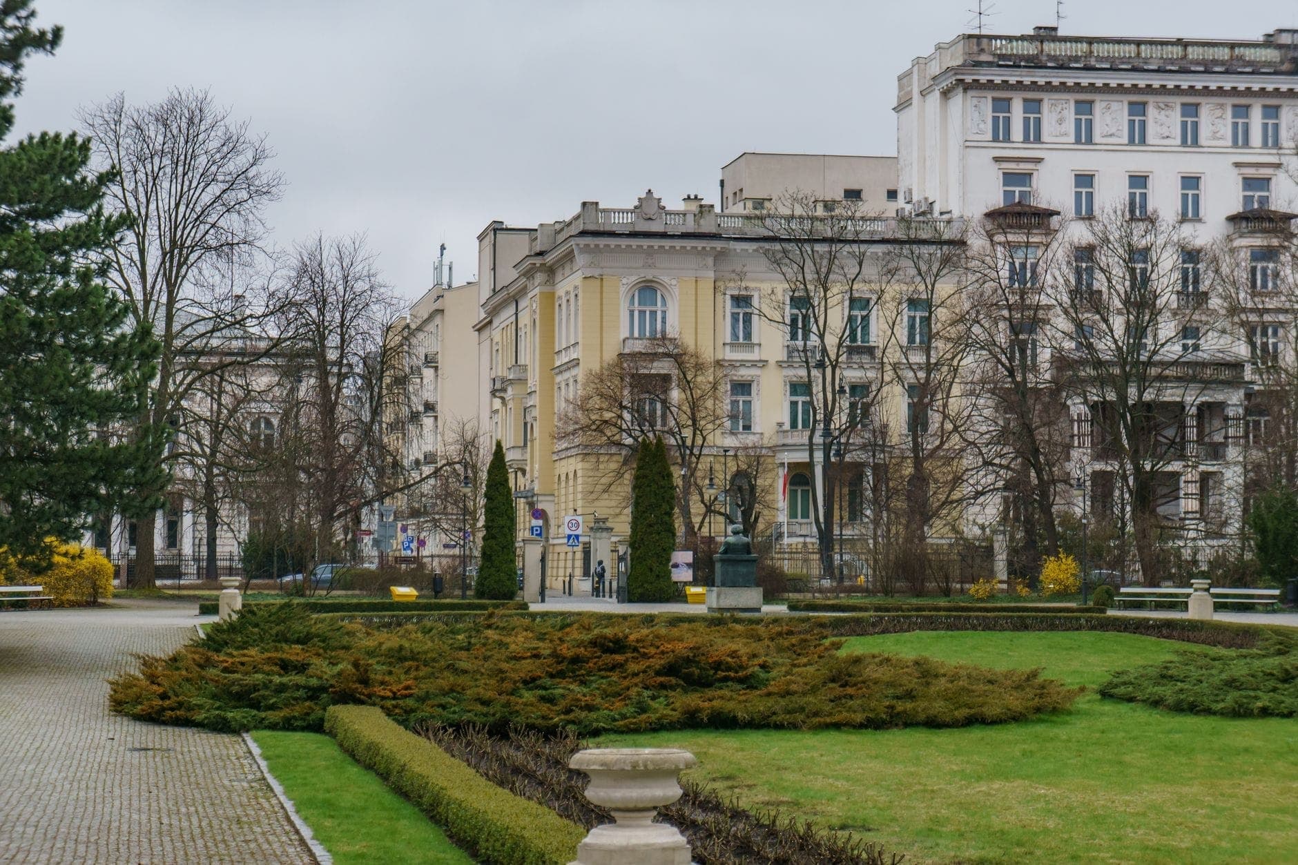Stadtpark in Warschau mit ordentlich gestutzten Hecken und stattlichen umliegenden Gebäuden an einem bewölkten Tag im Stadtzentrum.