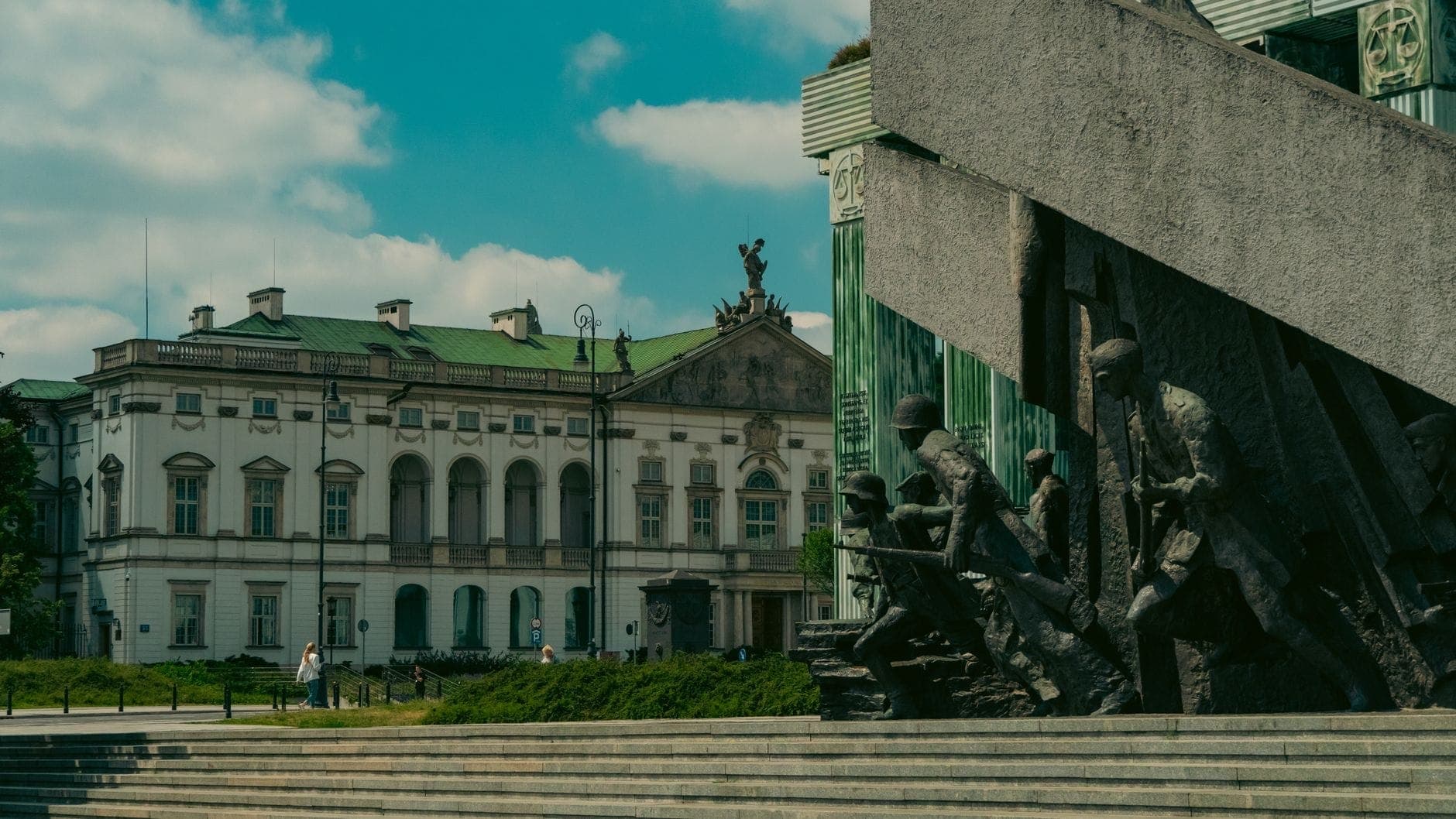 Großes Monument des Warschauer Aufstands mit dramatischen Bronzestatuen von Kämpfern vor einem neoklassizistischen Gebäude unter strahlendem Himmel in Warschau.