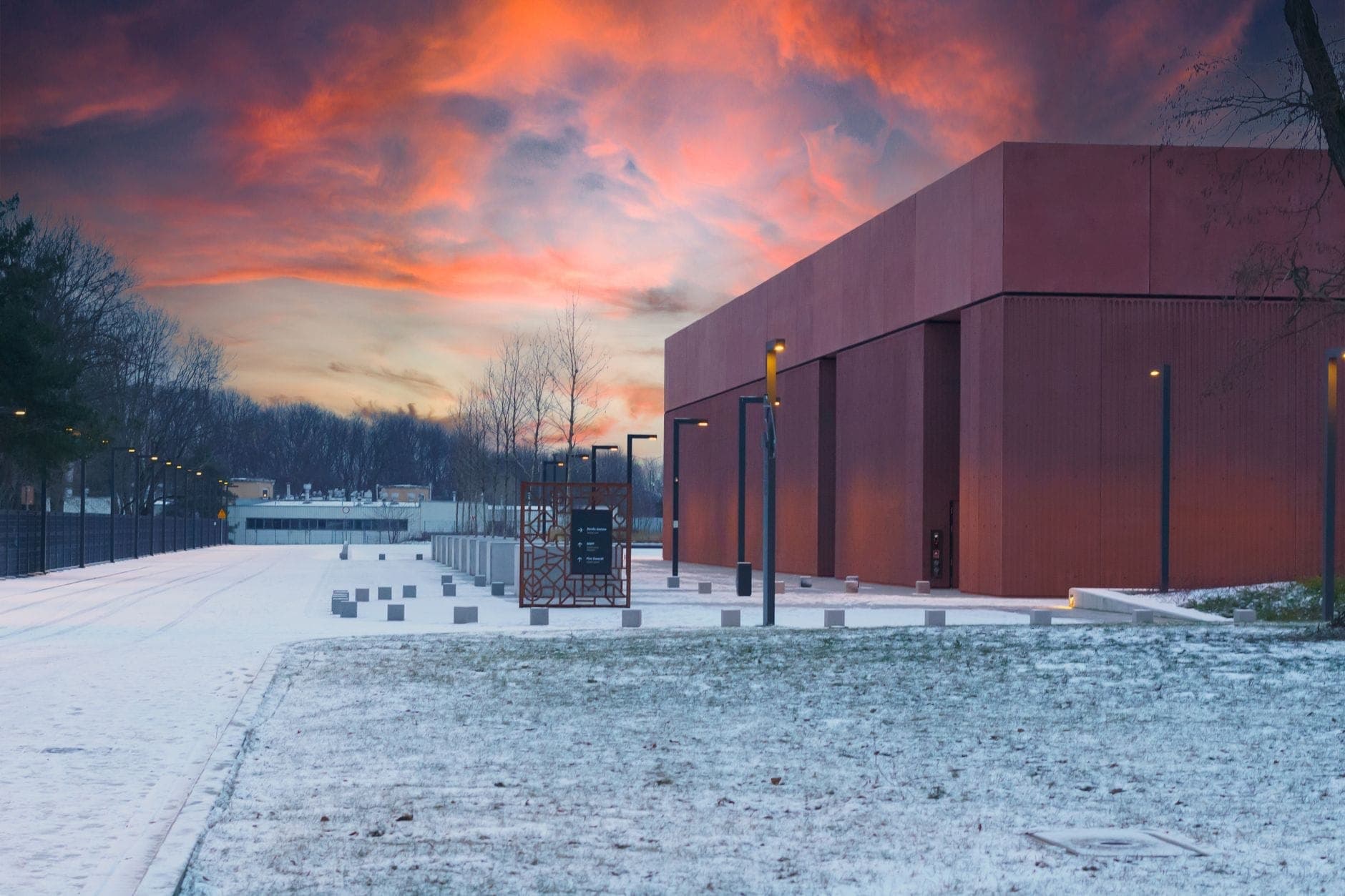 Façade moderne du musée de la prison Pawiak à Varsovie au coucher du soleil, avec une allée enneigée et un bâtiment minimaliste de couleur rouille.