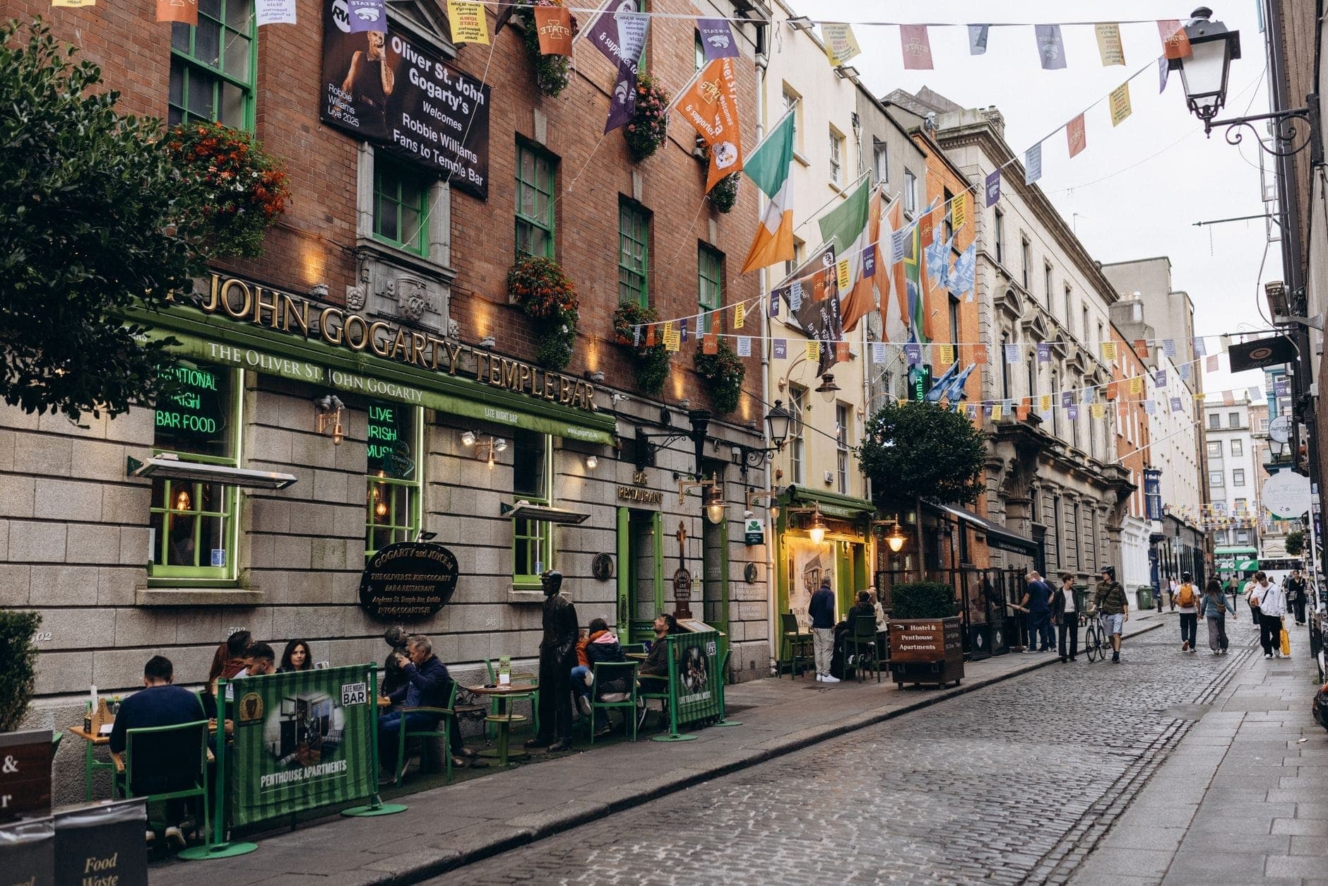 Una vivace strada di Dublino con tavoli all'aperto davanti a un tradizionale pub irlandese addobbato di bandiere e pieno di gente, che evoca la cultura gastronomica locale.