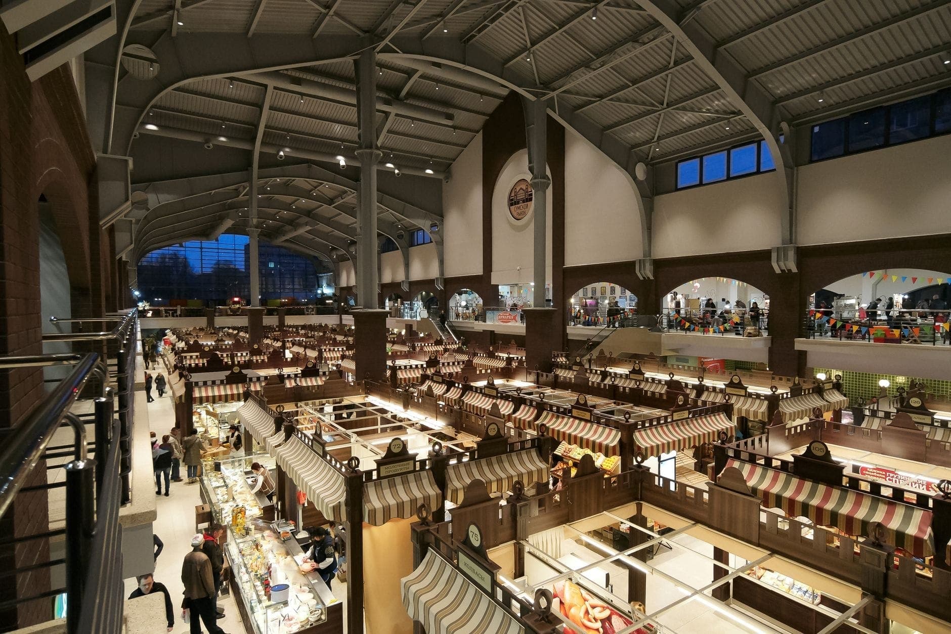 Innenansicht einer großen belebten Markthalle mit Reihen von Essensständen und einkaufenden Menschen in Warschau.