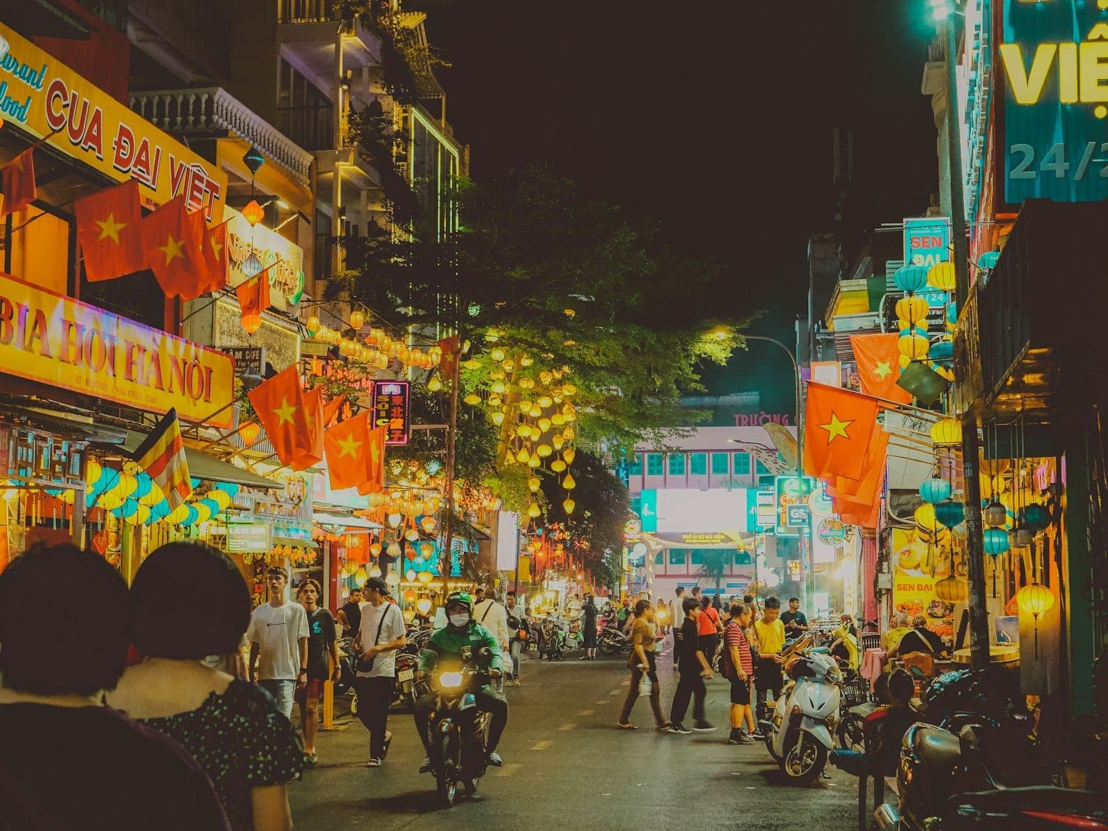Đường phố TP. Hồ Chí Minh nhộn nhịp về đêm với biển hiệu neon, người đi bộ, xe máy và các nhà hàng sáng đèn, ghi lại trọn vẹn không khí ẩm thực sôi động của thành phố.
