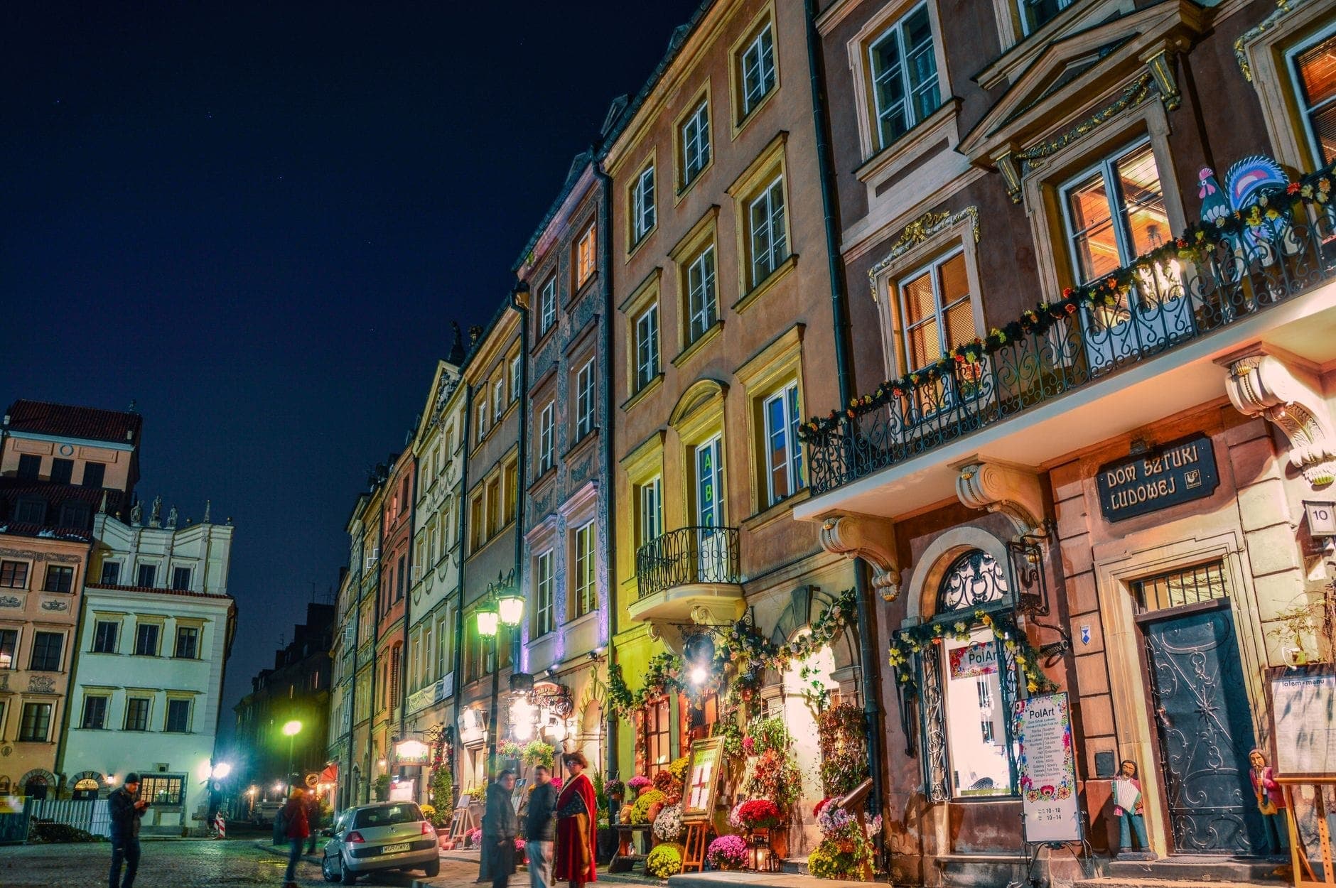 Nächtlicher Blick auf eine lebhafte Warschauer Straße, gesäumt von bunten historischen Gebäuden und einladenden, mit Blumen dekorierten Restaurants – ein Bild der lebendigen Gastronomieatmosphäre der Stadt.