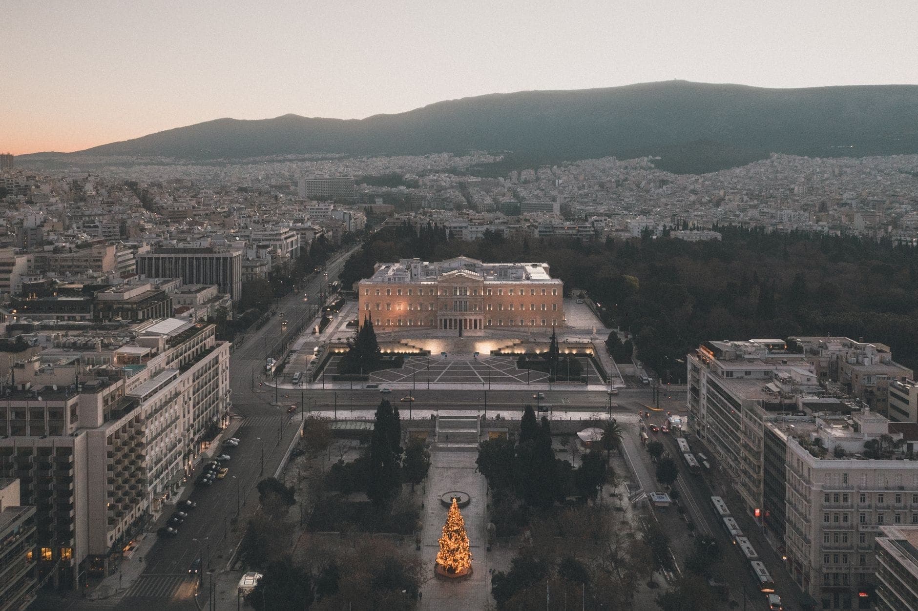 Vista aérea de la Plaza Syntagma con el edificio del Parlamento griego y el paisaje urbano circundante al atardecer en el centro de Atenas.