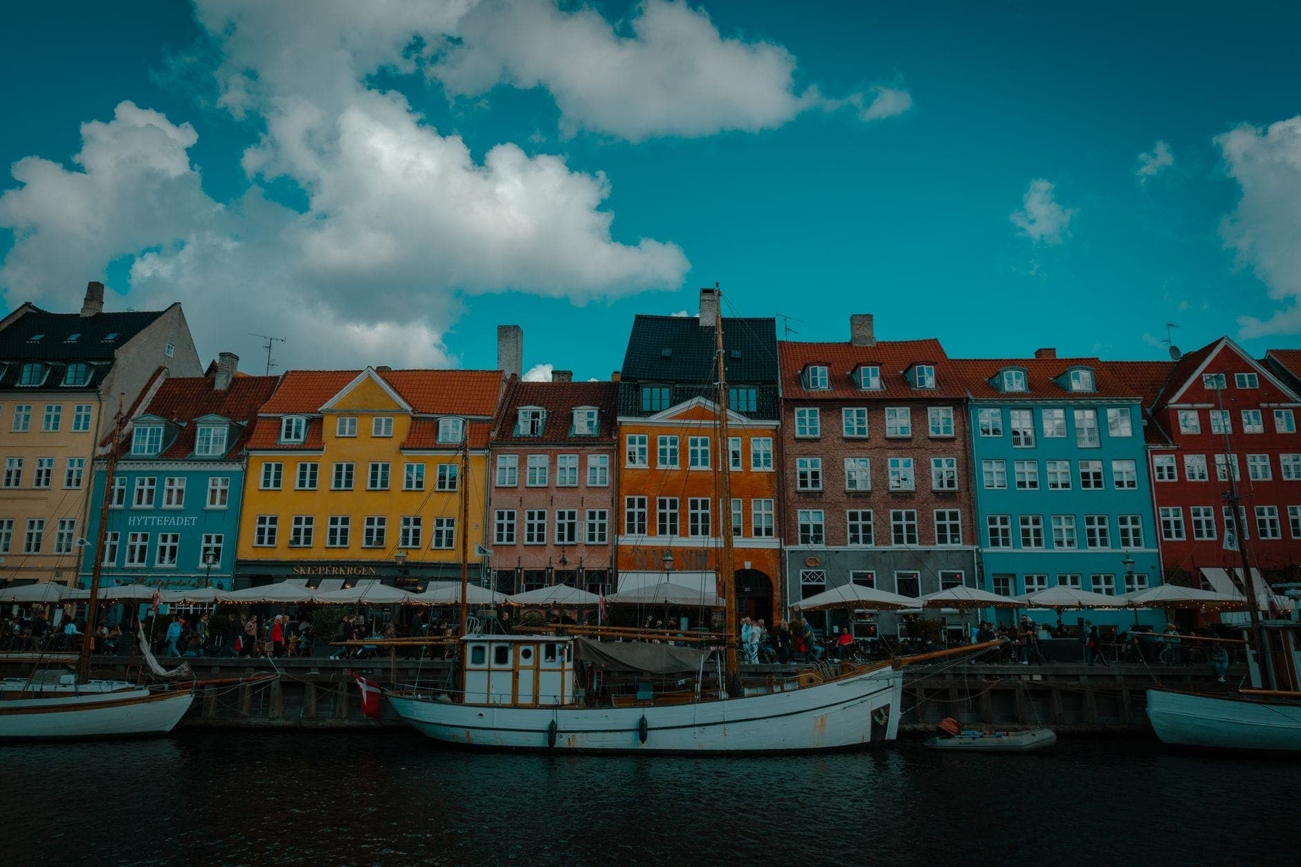 Bunte historische Häuser am Nyhavn-Kanal in Kopenhagen unter blauem Himmel mit vereinzelten Wolken, Boote vor der Uferpromenade, lebhafte Atmosphäre – perfekt als Reiseinspiration.