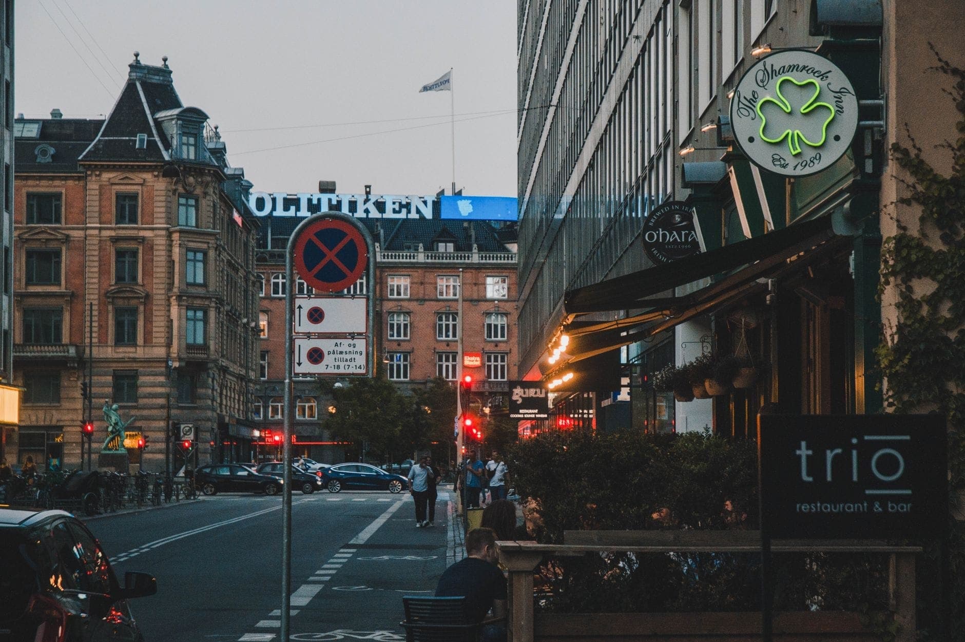 Abendliche Straßenszene im Vesterbro-Viertel in Kopenhagen mit Cafés, Leuchtreklamen, Fußgängern und historischen Gebäuden in der Nähe des Stadtzentrums.