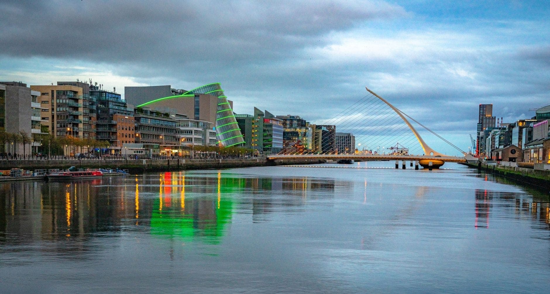 Vista panorámica del horizonte de Dublín a lo largo del río Liffey con el Puente Samuel Beckett y edificios modernos bajo un cielo luminoso al atardecer.