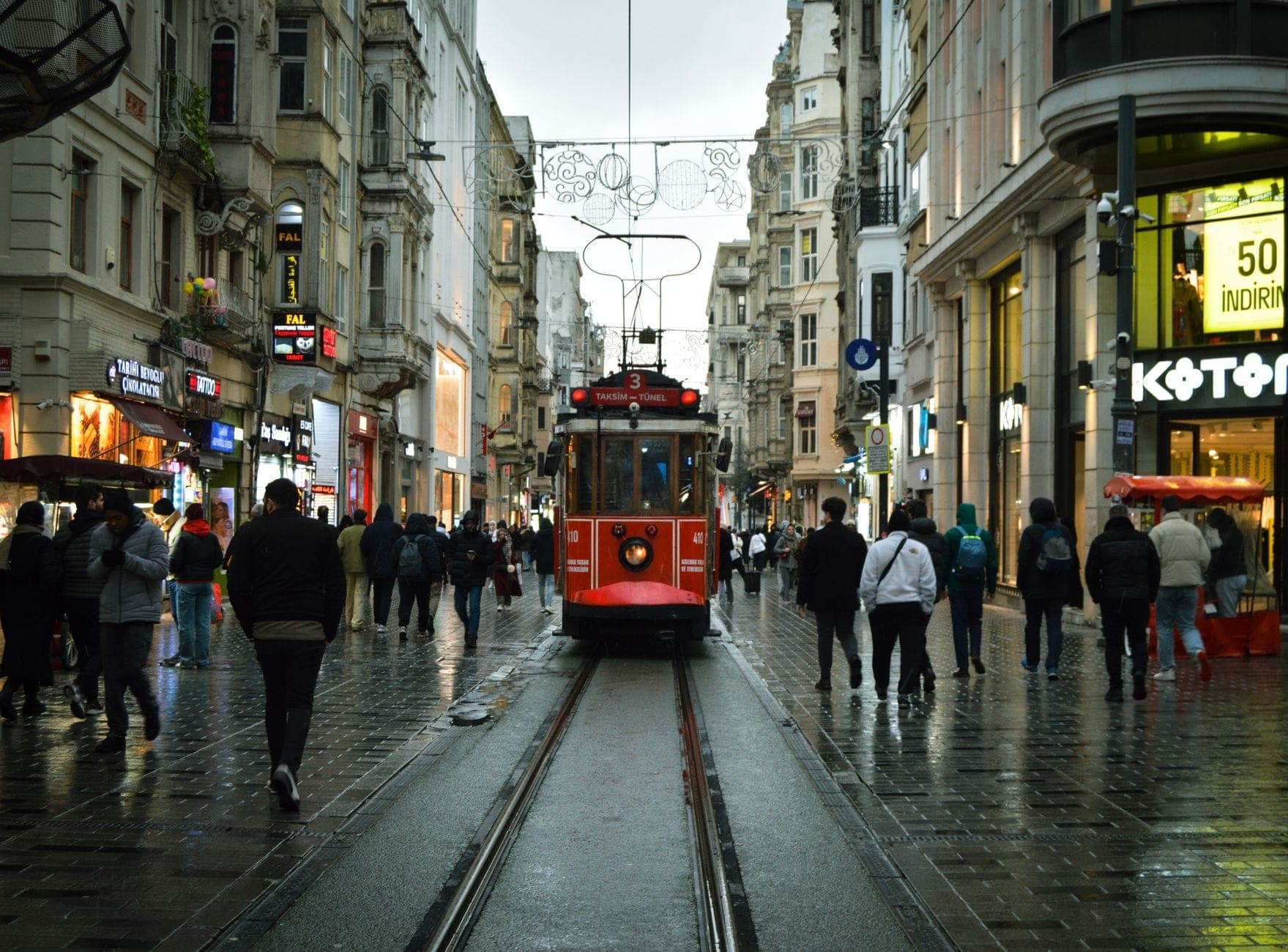 Vista lungo l'Avenue Istiklal di Istanbul a Beyoğlu con l'iconico tram rosso, pedoni, negozi ed edifici storici in una giornata piovosa.