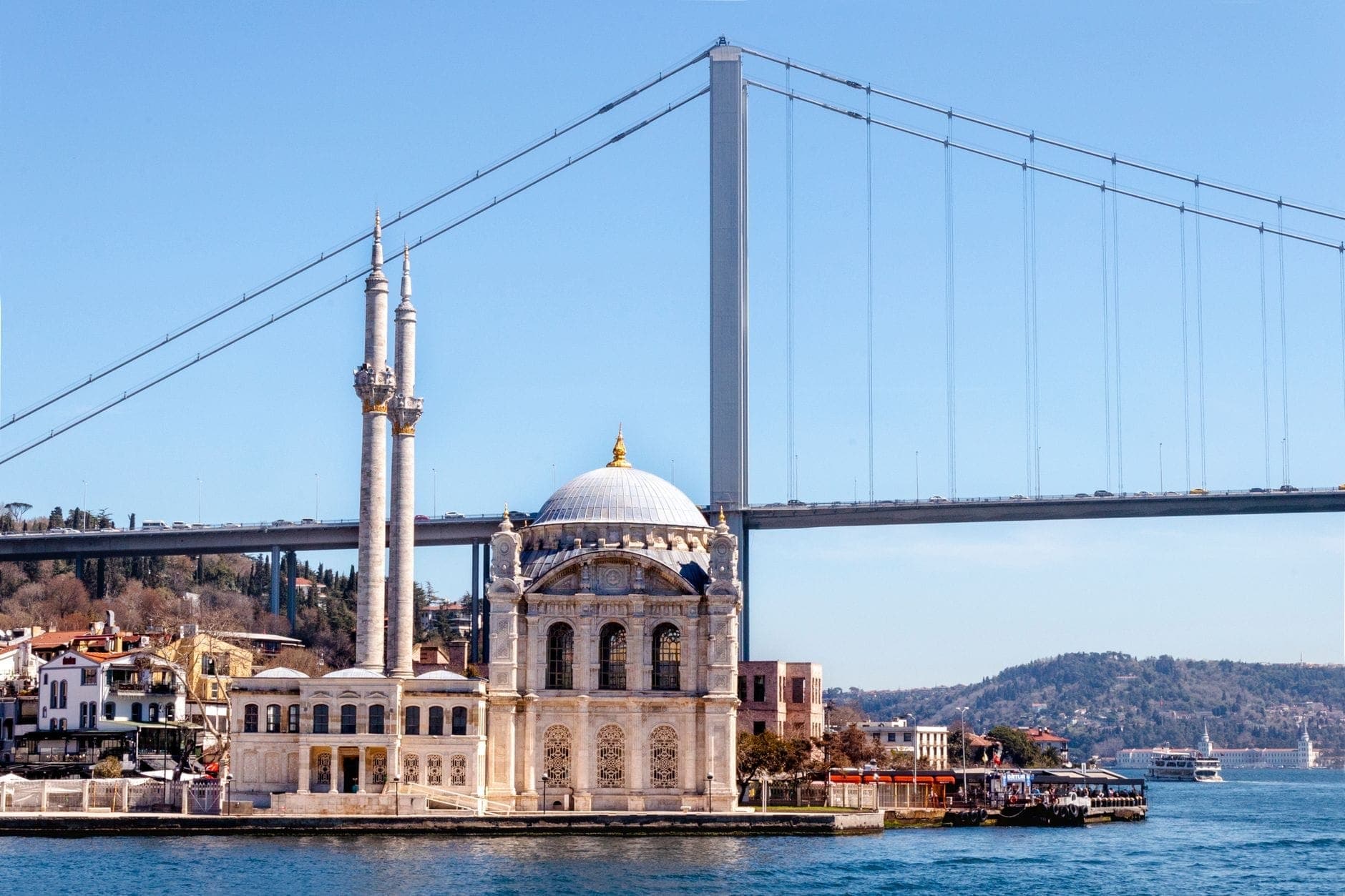 Elegante moschea sul lungomare del Bosforo con il Ponte del Bosforo sullo sfondo e cielo azzurro limpido.