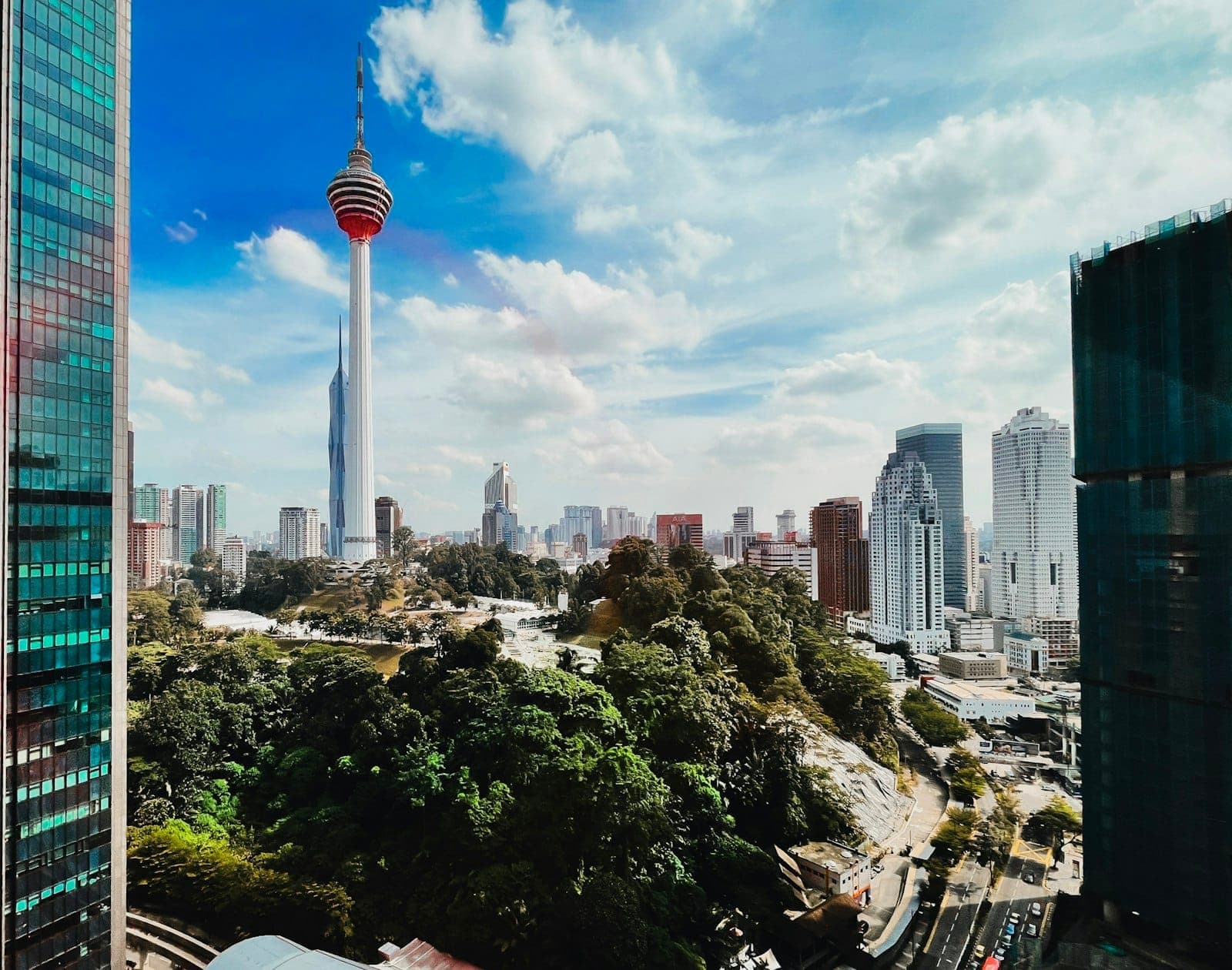 Toàn cảnh từ trên cao **Tháp đôi Petronas** vươn lên giữa đường chân trời Kuala Lumpur lúc hoàng hôn, bao quanh bởi ánh đèn thành phố nhộn nhịp.