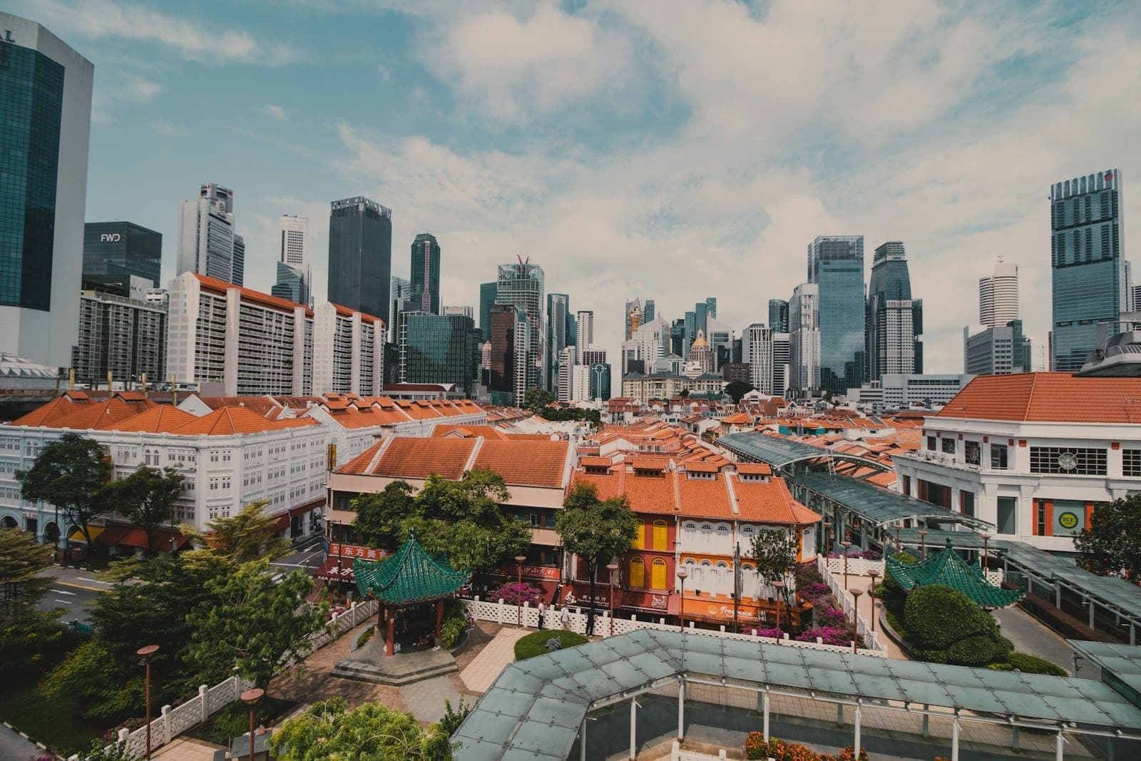 A sweeping view of Singapore’s city skyline, blending modern skyscrapers and historic shophouses with red roofs, highlighting diverse neighborhoods under a bright sky.