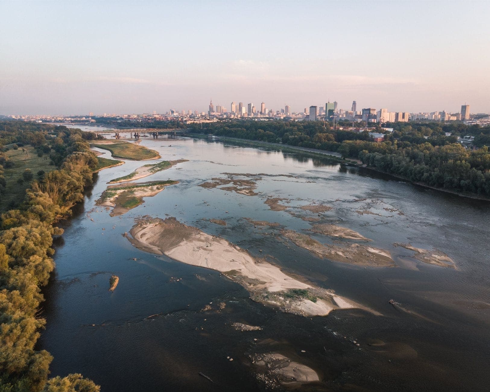 Luftaufnahme der Skyline von Warschau mit der Weichsel, die Grünflächen und Stadtgebäude auf beiden Ufern trennt.