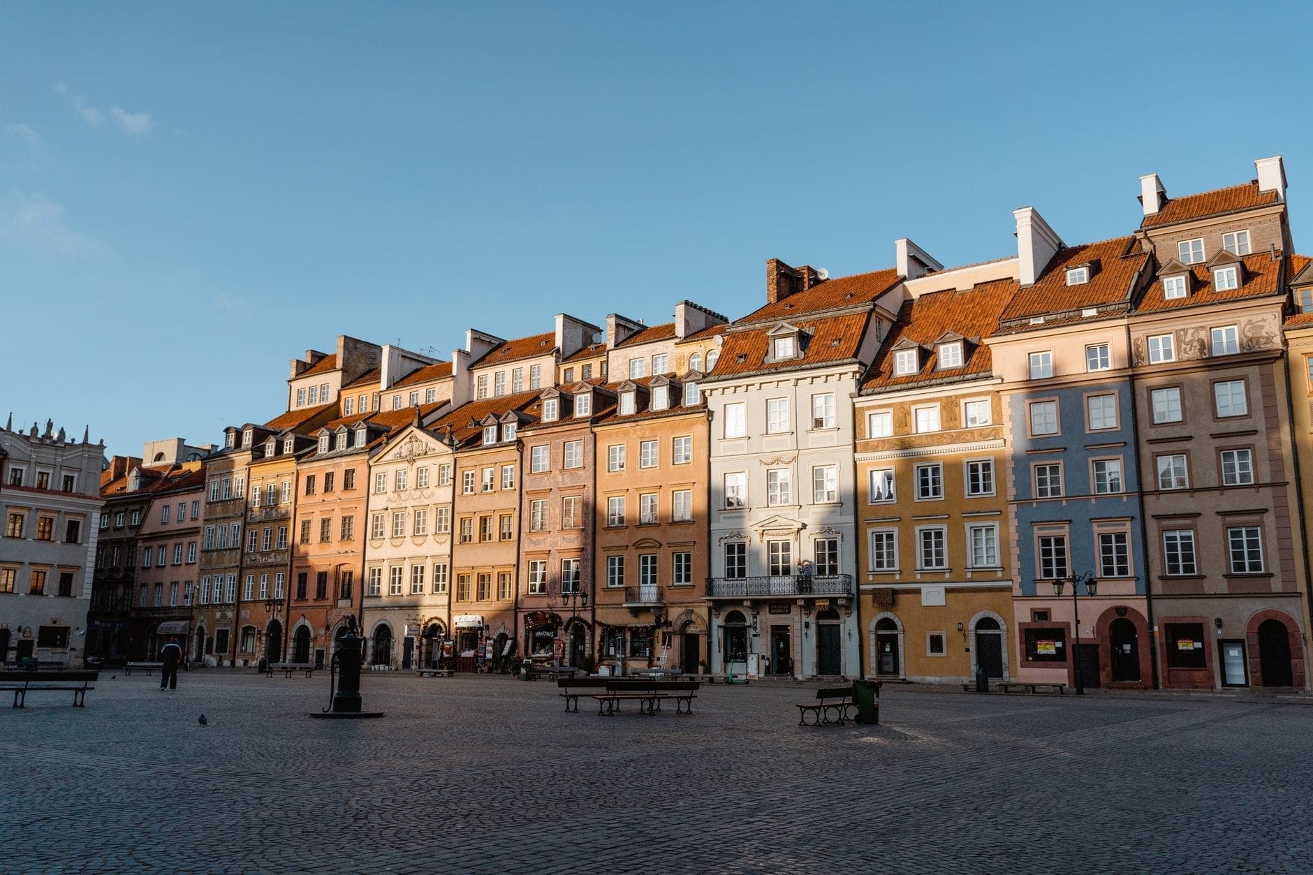 Weitläufiger Blick auf die bunten historischen Bürgerhäuser rund um den sonnendurchfluteten Marktplatz in Warschaus Altstadt – lebendige Atmosphäre und einladende Architektur.