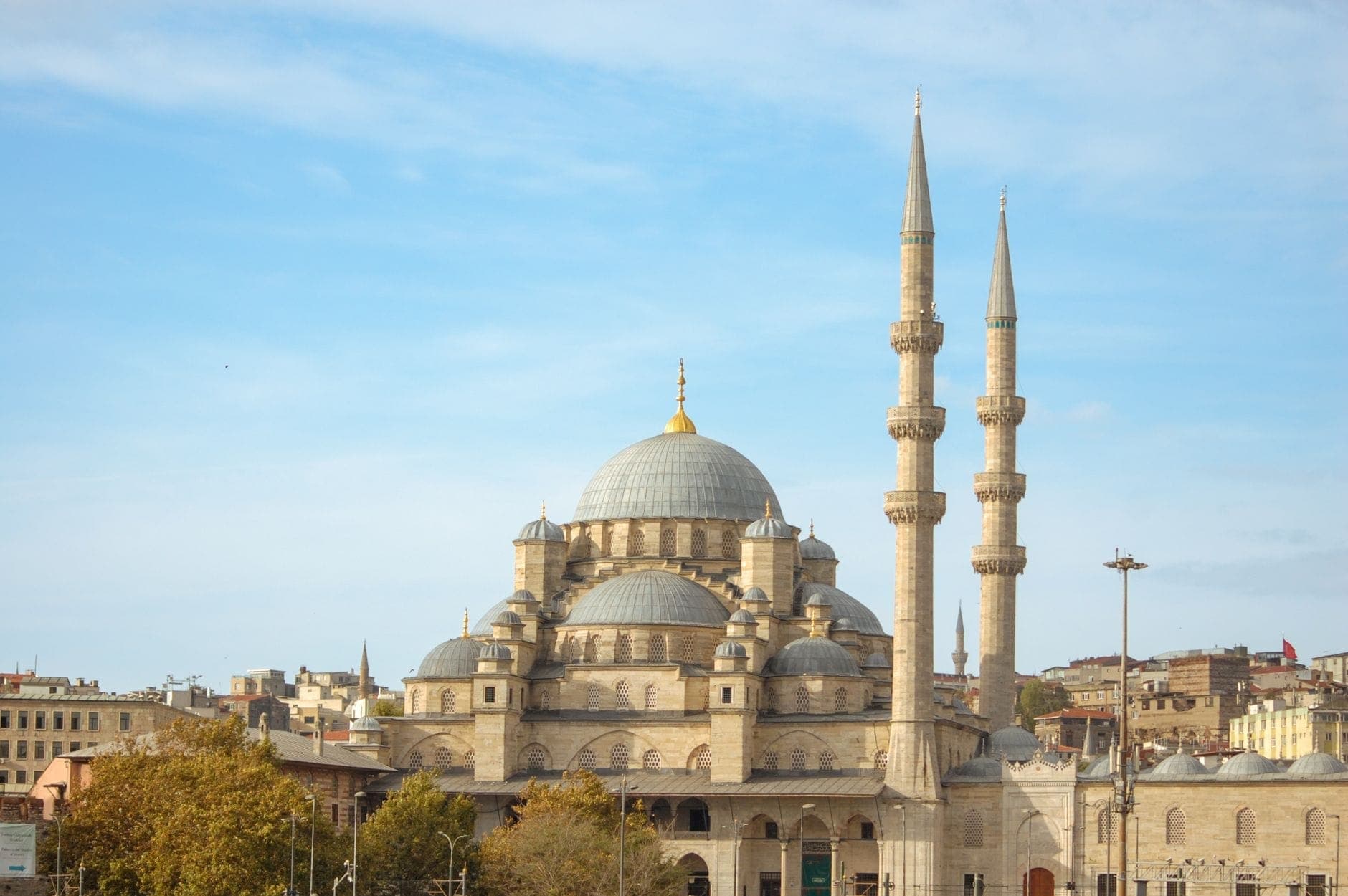 Weitwinklige Ansicht der Yeni Cami (Neue Moschee) mit ihren mächtigen Kuppeln und zwei schlanken Minaretten, die über dem geschäftigen Eminönü unter klarem blauem Himmel aufragen.