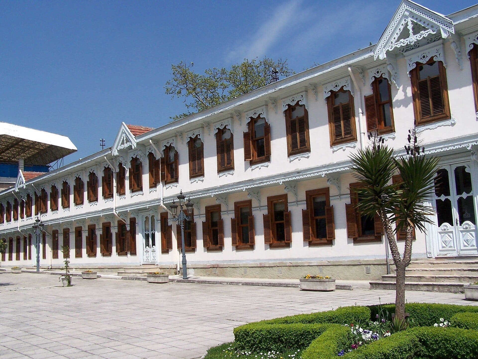 Hauptgebäude des Yıldız Palace mit weißer Fassade, Holzläden und kunstvollen Verzierungen, umgeben von gepflegten Gärten unter einem strahlend blauen Himmel.